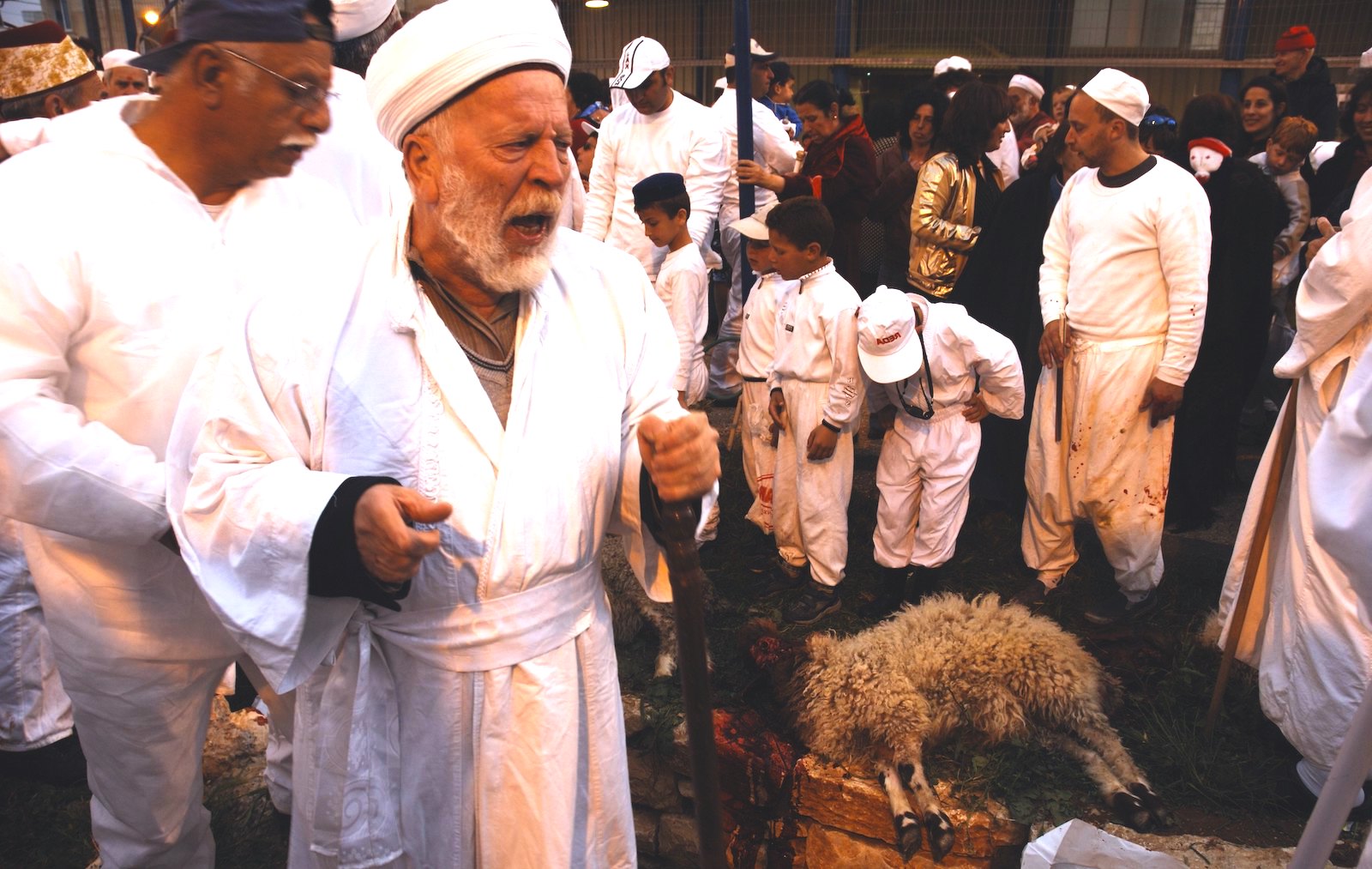 Man in a robe with an intense look on his face next to a slaughtered sheep with a crowd of peple.
