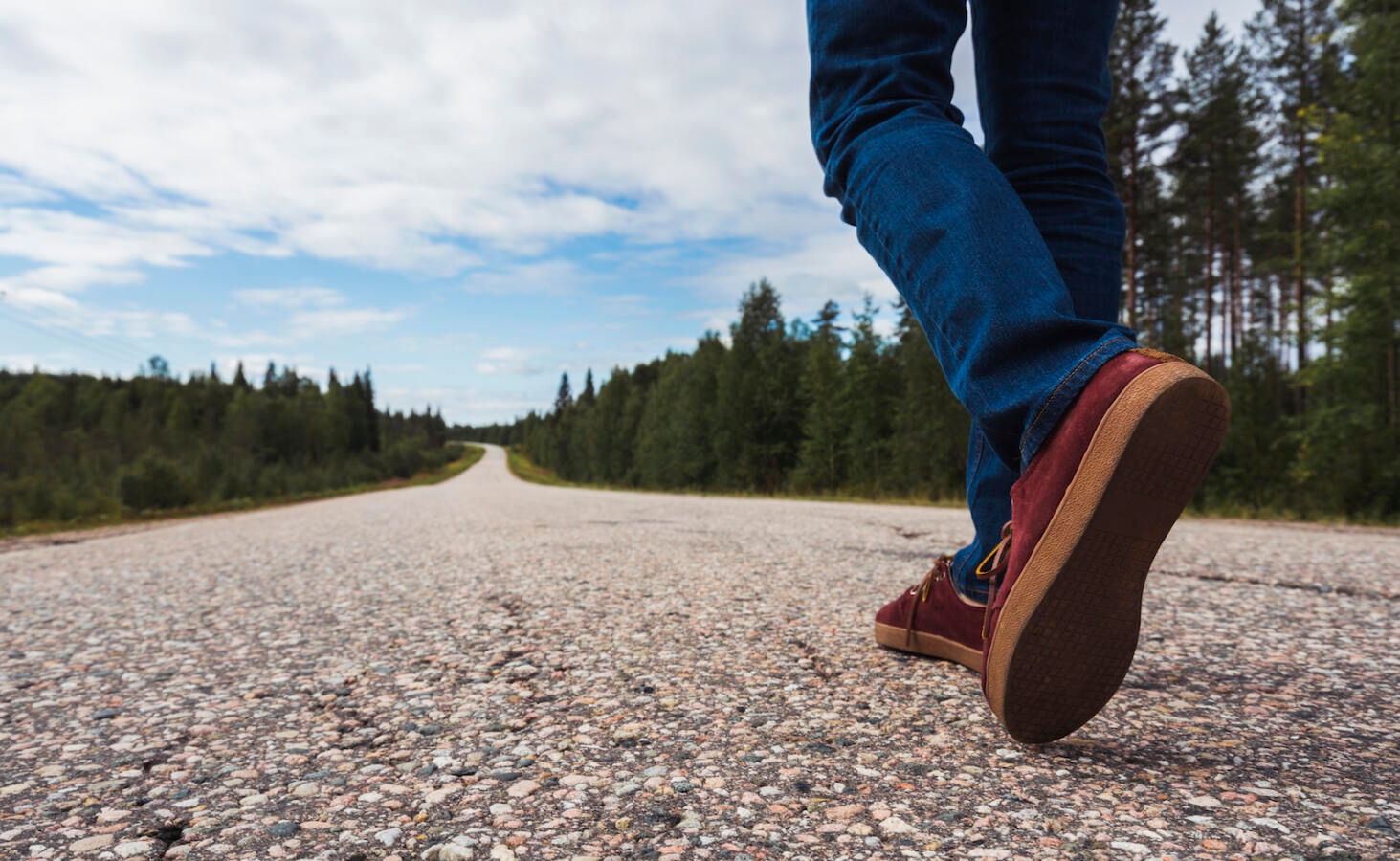 Finland, Lapland, feet of man walking on empty country road