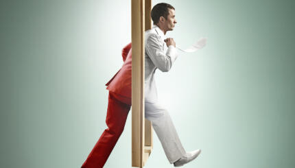 A young man steps through a doorway and the color of his suit changes from one side to the other.