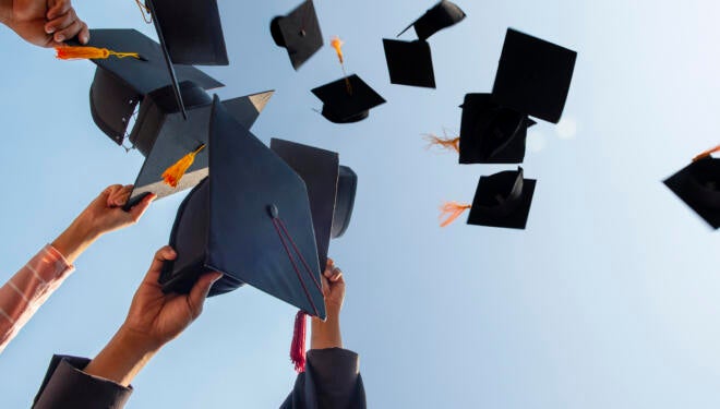 People Throwing Mortarboards Against Clear Sky