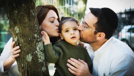 Photo of a Jewish couple kissing their child.