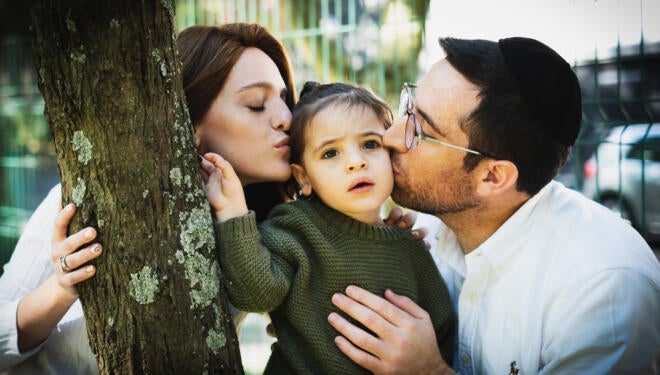 Photo of a Jewish couple kissing their child.