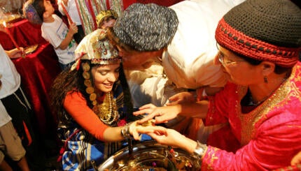 A richly-adorned bride whose hand is being annointed with henna.