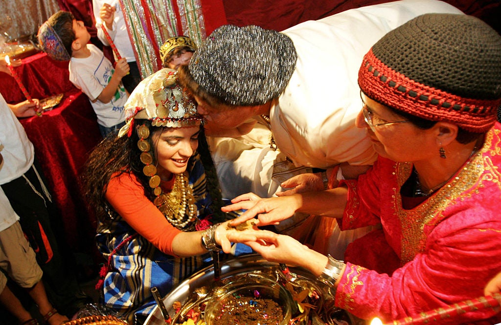 A richly-adorned bride whose hand is being annointed with henna.